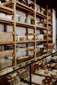 A bakery display with shelves filled with various containers and wooden boxes. The counter is lined with a variety of freshly baked goods, including muffins and pastries. The setting has a rustic and cozy atmosphere with wooden shelves and glass display cases.