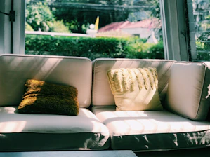 A fabric sofa bed styled with knitted throw pillows in a sunlit rustic living room.