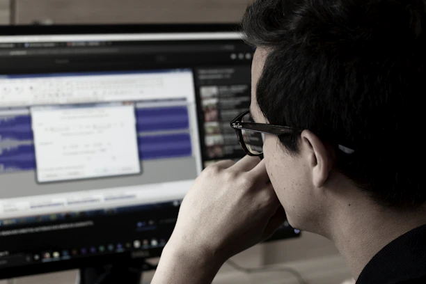 A focused professional typing on a laptop with audio waveforms displayed on screen.