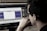 A person wearing glasses is deeply focused on a computer screen displaying audio editing software. The screen shows waveforms and various controls while the room has a dim, professional atmosphere.