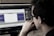A person wearing glasses is deeply focused on a computer screen displaying audio editing software. The screen shows waveforms and various controls while the room has a dim, professional atmosphere.