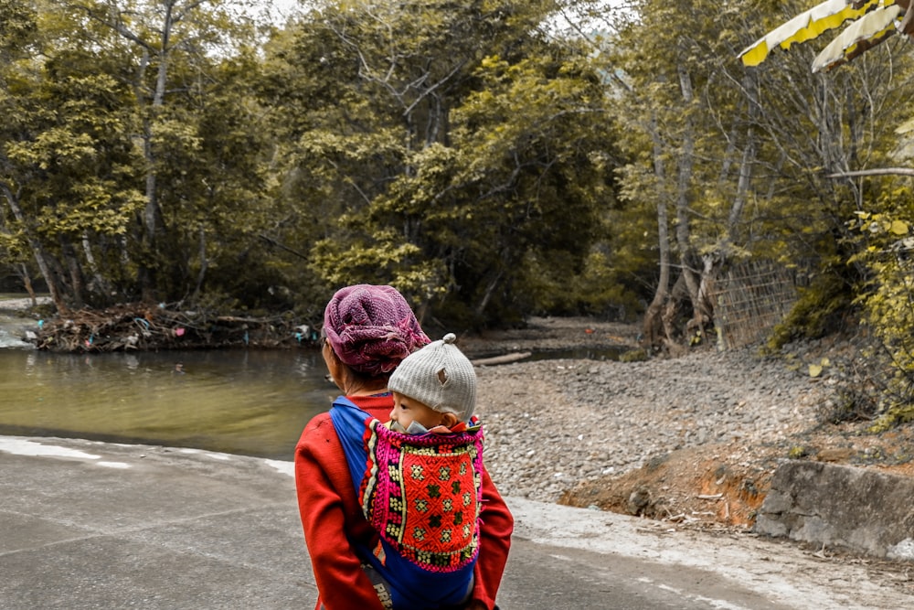 woman carrying baby on back walking near lake