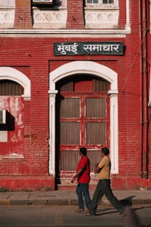 2 men walking past red building