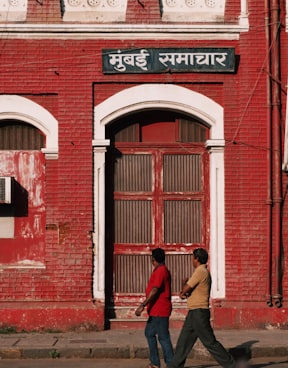 2 men walking past red building