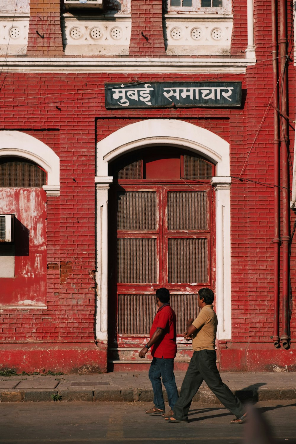 2 men walking past red building