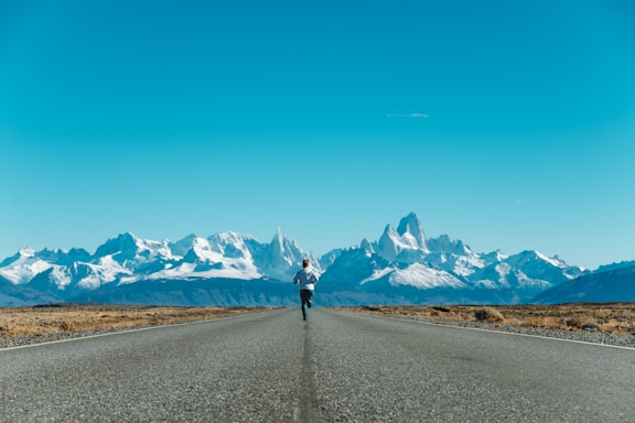 A runner crossing the finish line with mountains in the background under a clear blue sky.