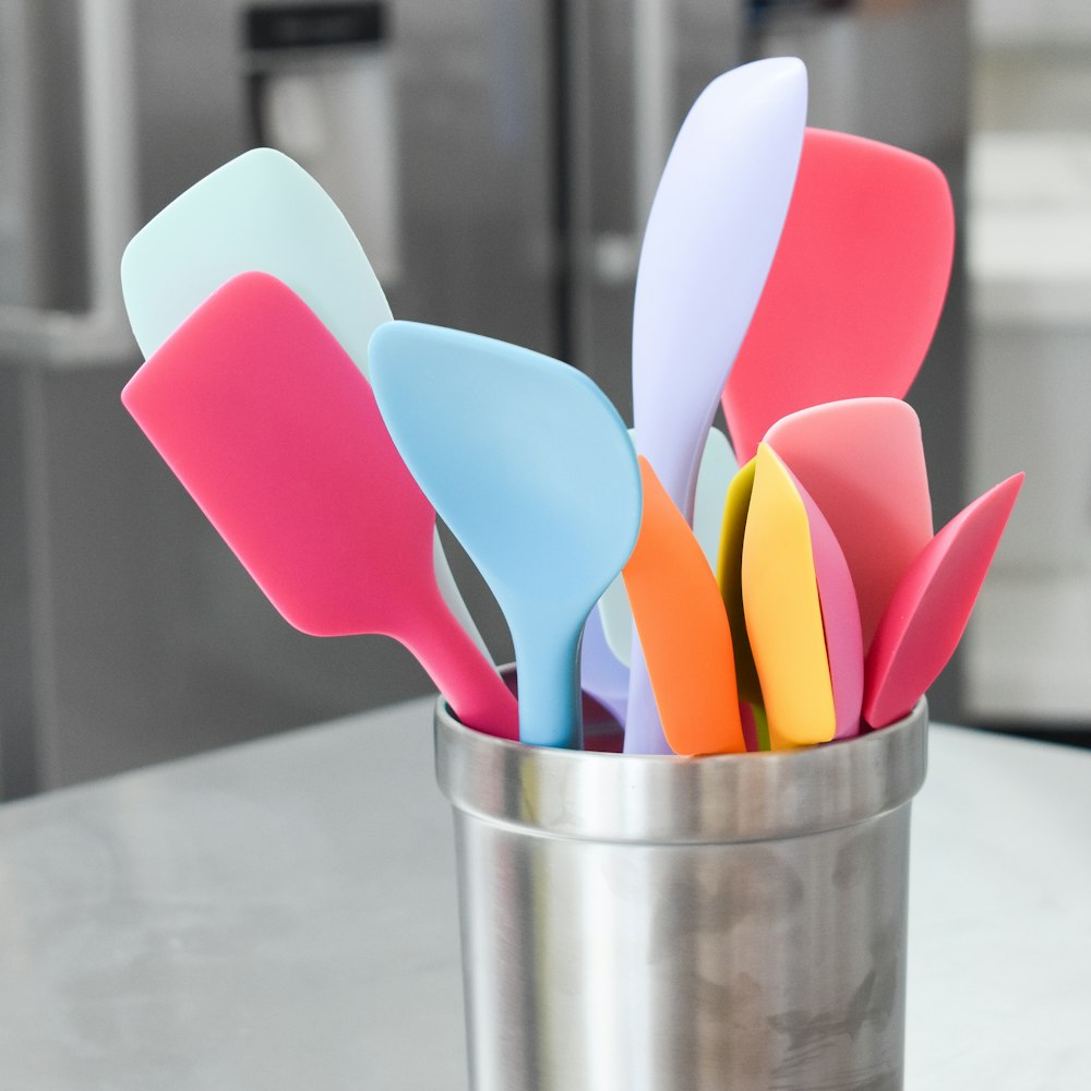 Mestoli di plastica rosa, blu e bianchi in contenitore inox