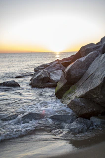 Sunset casting warm hues over a tranquil beach cove with smooth rocks and soft waves.