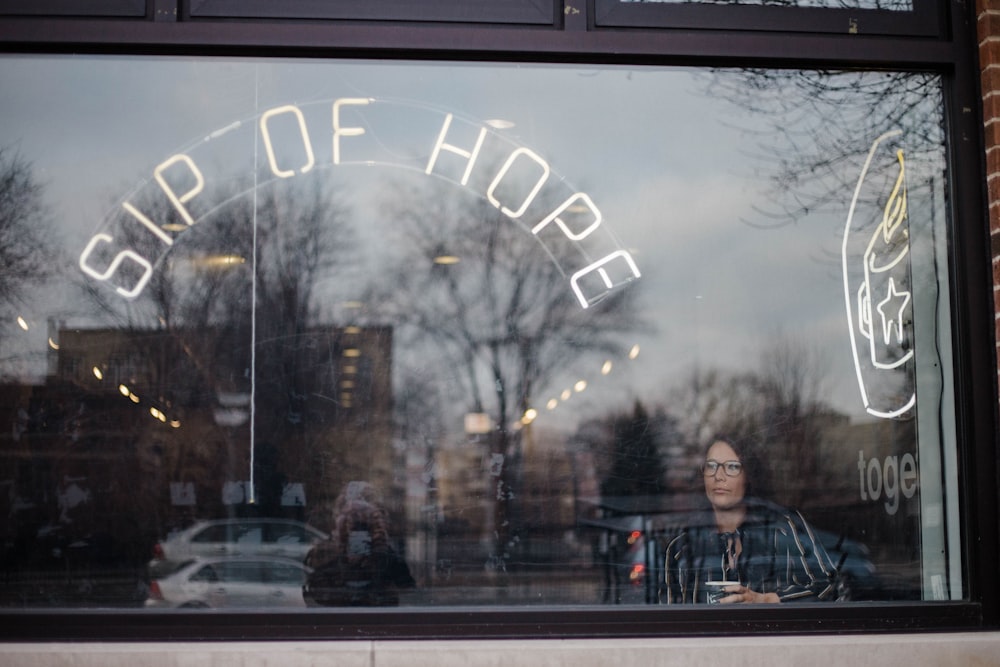 woman in black striped shirt looking outside through glass window at coffee shop