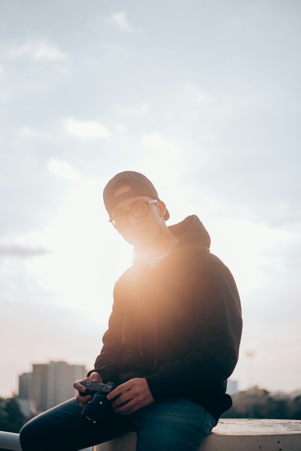 man in black hoodie sitting on railings holding camera