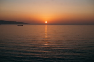 A serene image of a ship sailing across a calm sea at sunset.