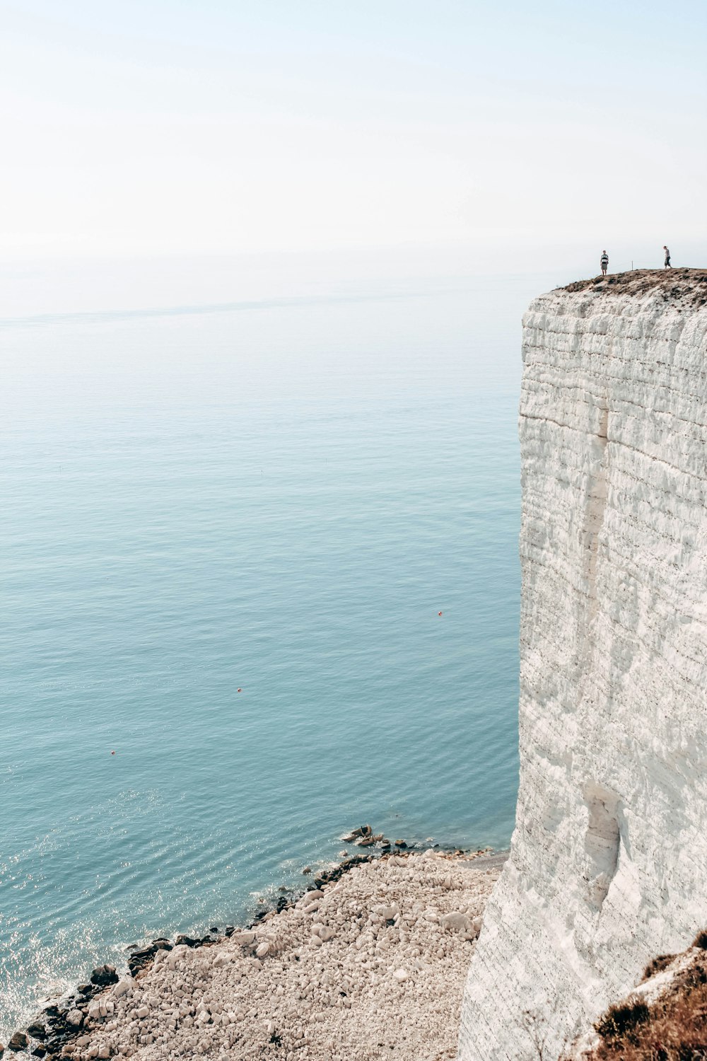 two person standing on rock cliff beside body of water