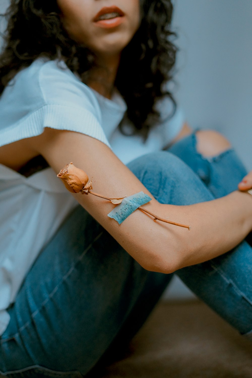 woman wearing blue denim jeans sitting with brown rose on her arm