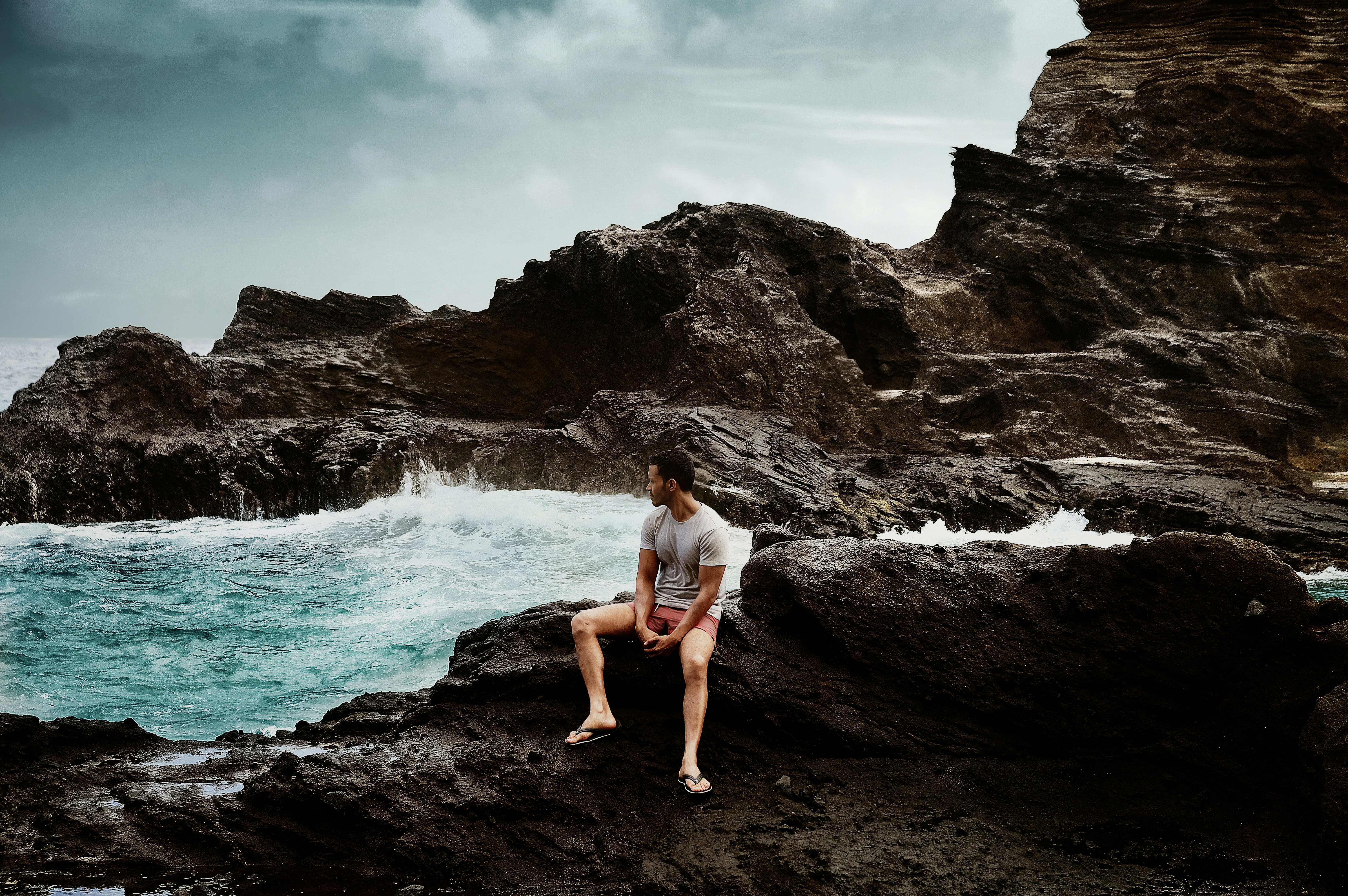 man in shirt sitting on rock formation, 