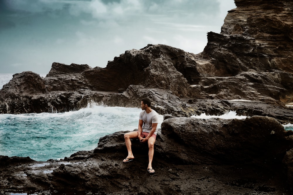 man in shirt sitting on rock formation