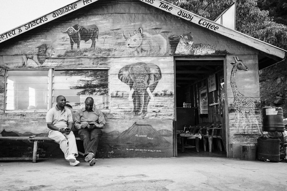 Graustufenfotografie von zwei Männern, die auf einer Bank sitzen