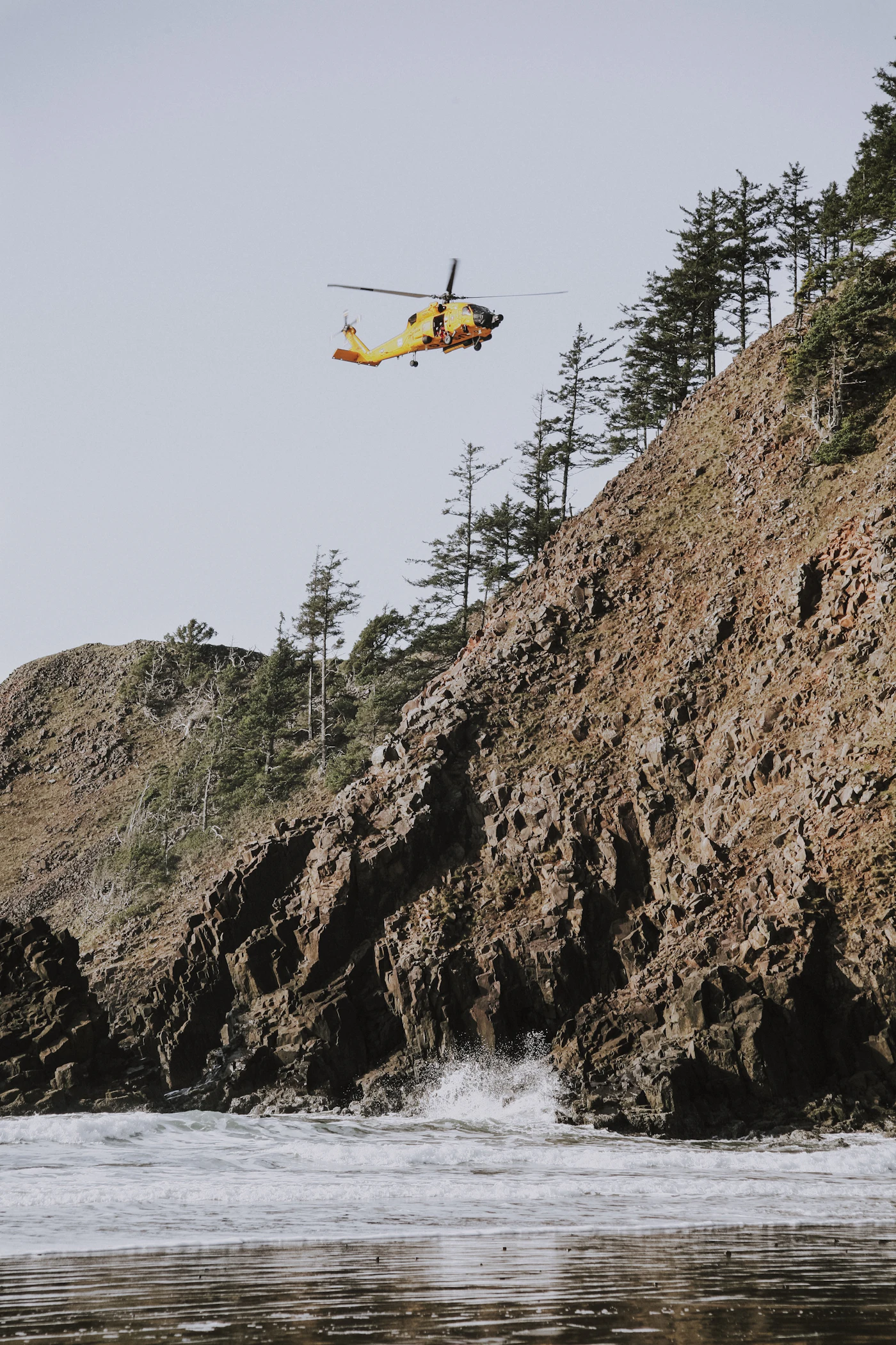 A helicopter flying low over grey water near a shoreline