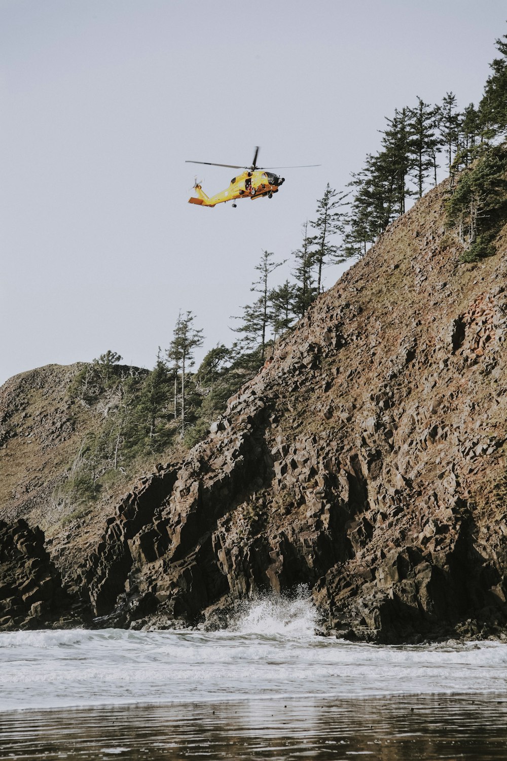 helicopter flying over body of water beside hill