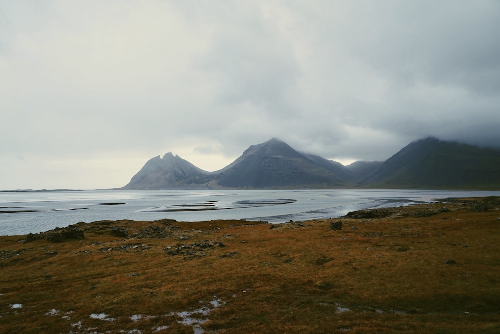 waves crashing on shore overlooking mountains under cloudy sky