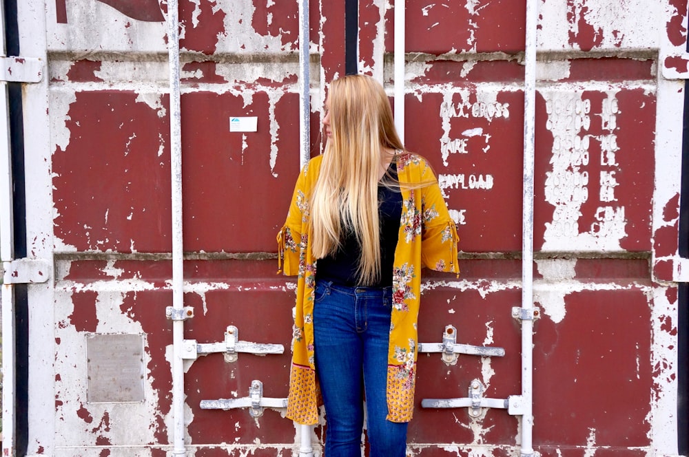woman wearing yellow cardigan leaning on red and white wall