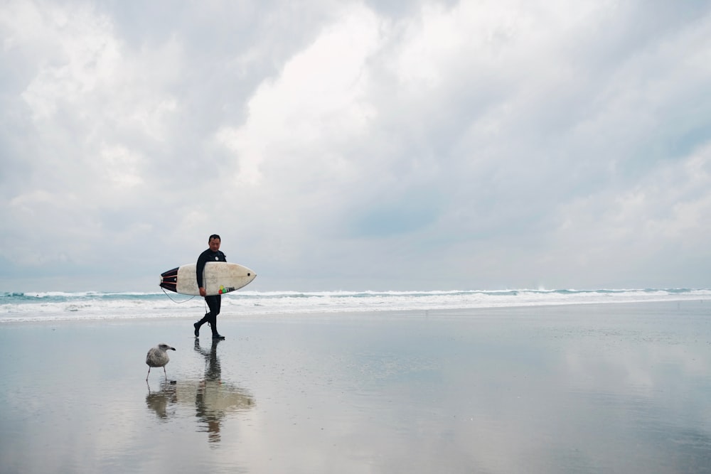 man walking on sea shore carrying surfboard