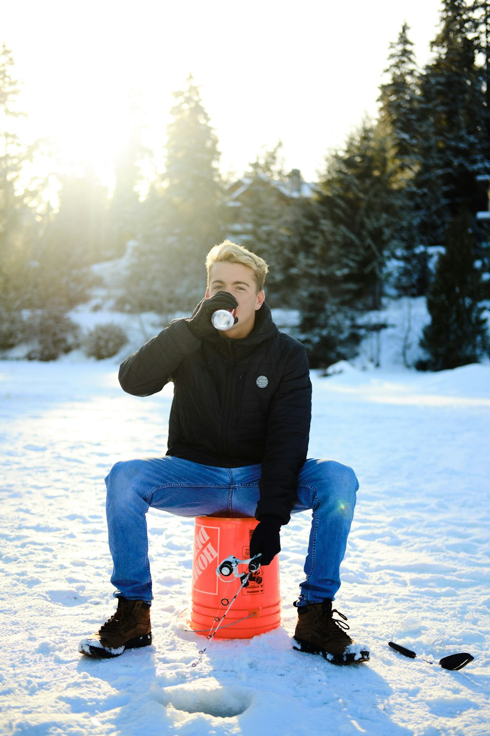 man drinking can sitting on orange bucket during daytime