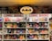 A comic book store display featuring numerous comic books on shelves, with a prominent neon Batman logo at the top. The shelves are labeled with signs reading 'Comic Books' in bright red letters. Various comic book covers with vibrant illustrations are visible, showcasing different characters and themes.