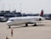 A Delta Air Lines aircraft on the tarmac at an airport, with a ground crew member in a bright orange vest directing it. The background includes an airport terminal and other parked vehicles.