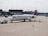 A commercial airplane is parked on an airport tarmac near a terminal. It's a Delta aircraft being guided by a ground crew member in an orange vest. The plane is attached to a tow vehicle at the front, preparing for taxi or maintenance. Various airport equipment and vehicles are present in the background, along with the terminal building.