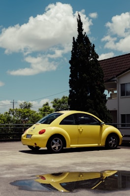 A bright yellow compact car parked on the lot of loja de veiculos under clear blue skies.