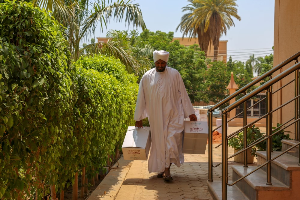 man walking beside green-leafed plants while carrying boxes