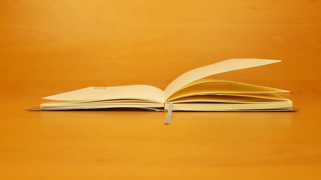 Aufgeschlagenes Notizbuch in Seitenansicht vor warm-orangefarbenem Hintergrund