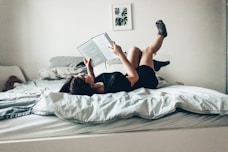 woman in black dress lying on bed while reading book
