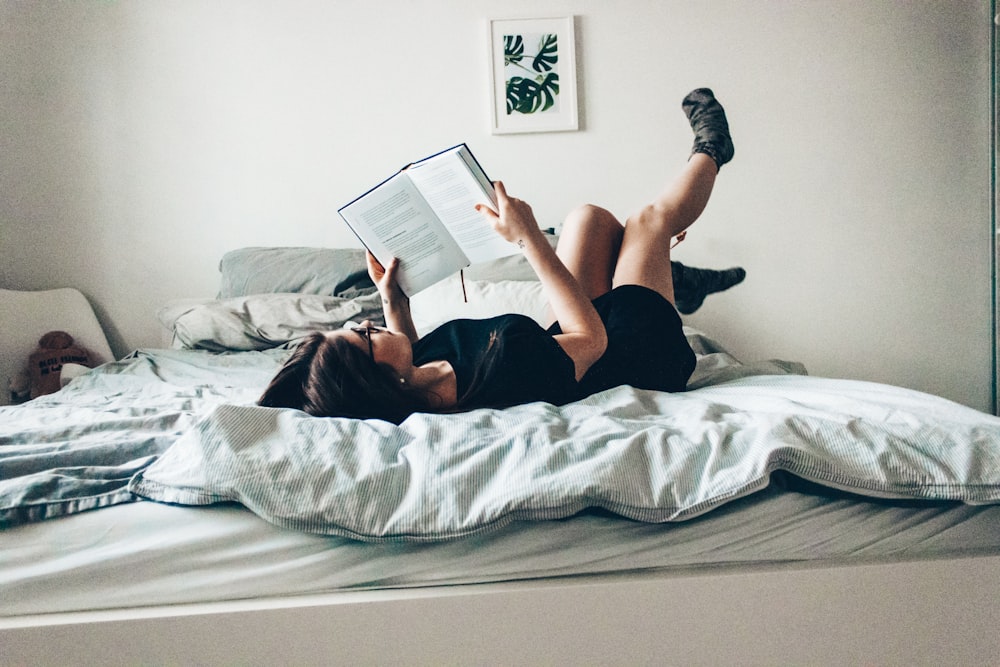 woman in black dress lying on bed while reading book