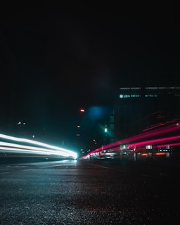 An urban night scene with stark white light trails weaving through a cityscape painted in electric orange hues