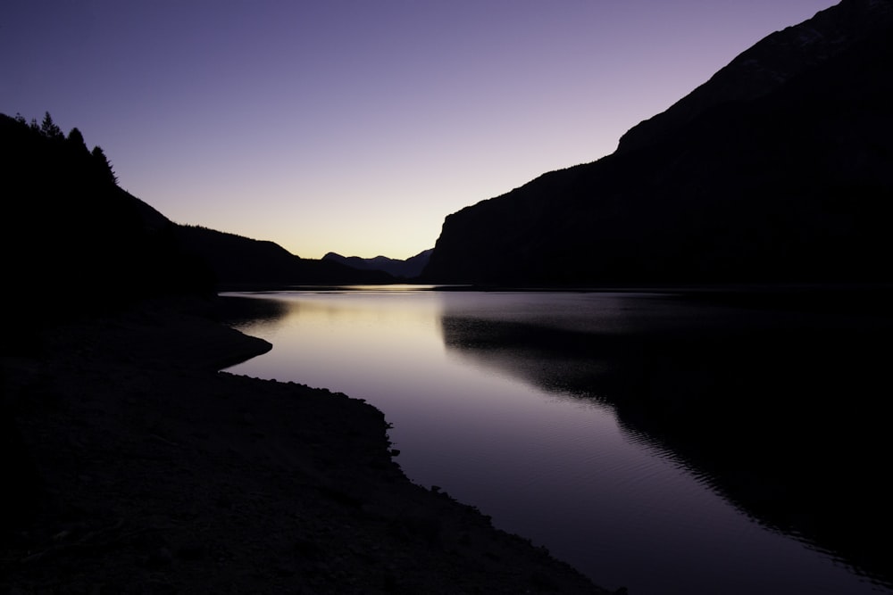 silhouette of hills on both banks of placid river reflecting purple sky light