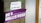 A concrete pillar features two signs taped to it. The top sign is white with the words 'WiFi Password: WE WANT MORE' printed in purple. Below it, a larger purple banner displays Korean text in white, translated as 'Welcome to Feminist Utopia.'