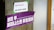 A concrete pillar features two signs taped to it. The top sign is white with the words 'WiFi Password: WE WANT MORE' printed in purple. Below it, a larger purple banner displays Korean text in white, translated as 'Welcome to Feminist Utopia.'