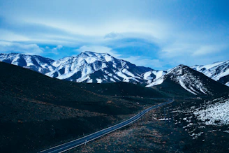 Snow-capped Atlas Mountains towering above a winding road with a Sellam Tours vehicle.