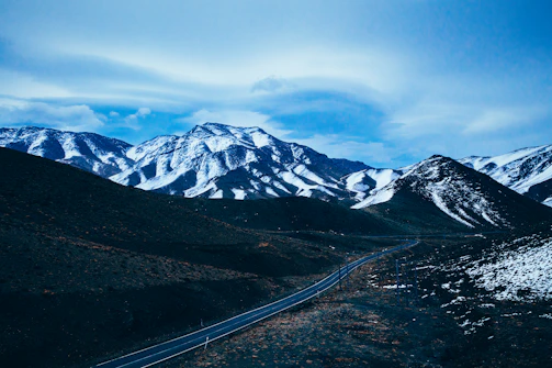 Snow-capped Atlas Mountains towering above a winding road with a Sellam Tours vehicle.