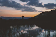 A woman standing at the edge of a turquoise mountain lake, arms wide open to the sky.