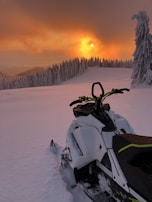 A sunset view over a frozen lake with a snowmobile parked at the edge, casting long shadows.