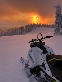 A sunset view over a frozen lake with a snowmobile parked at the edge, casting long shadows.