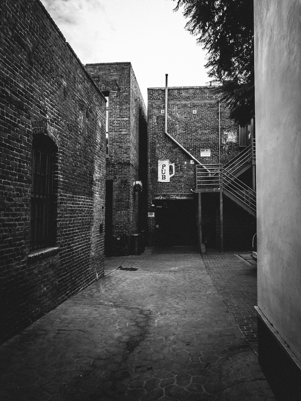 grayscale photography of alley with brick buildings