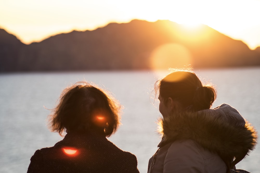 2 people standing in beach enjoying view of setting sun