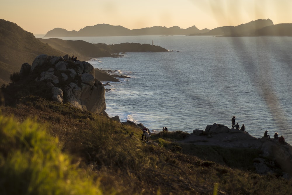 people on rock beside body of water