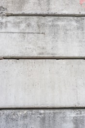 Several large, rectangular concrete slabs arranged horizontally, displaying a mottled gray texture with natural imperfections and speckles.