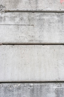 Several large, rectangular concrete slabs arranged horizontally, displaying a mottled gray texture with natural imperfections and speckles.
