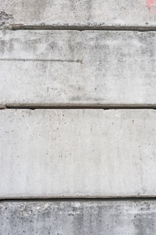 Several large, rectangular concrete slabs arranged horizontally, displaying a mottled gray texture with natural imperfections and speckles.