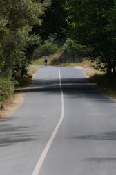 A rider testing a custom-built bike on a quiet, winding road surrounded by trees.
